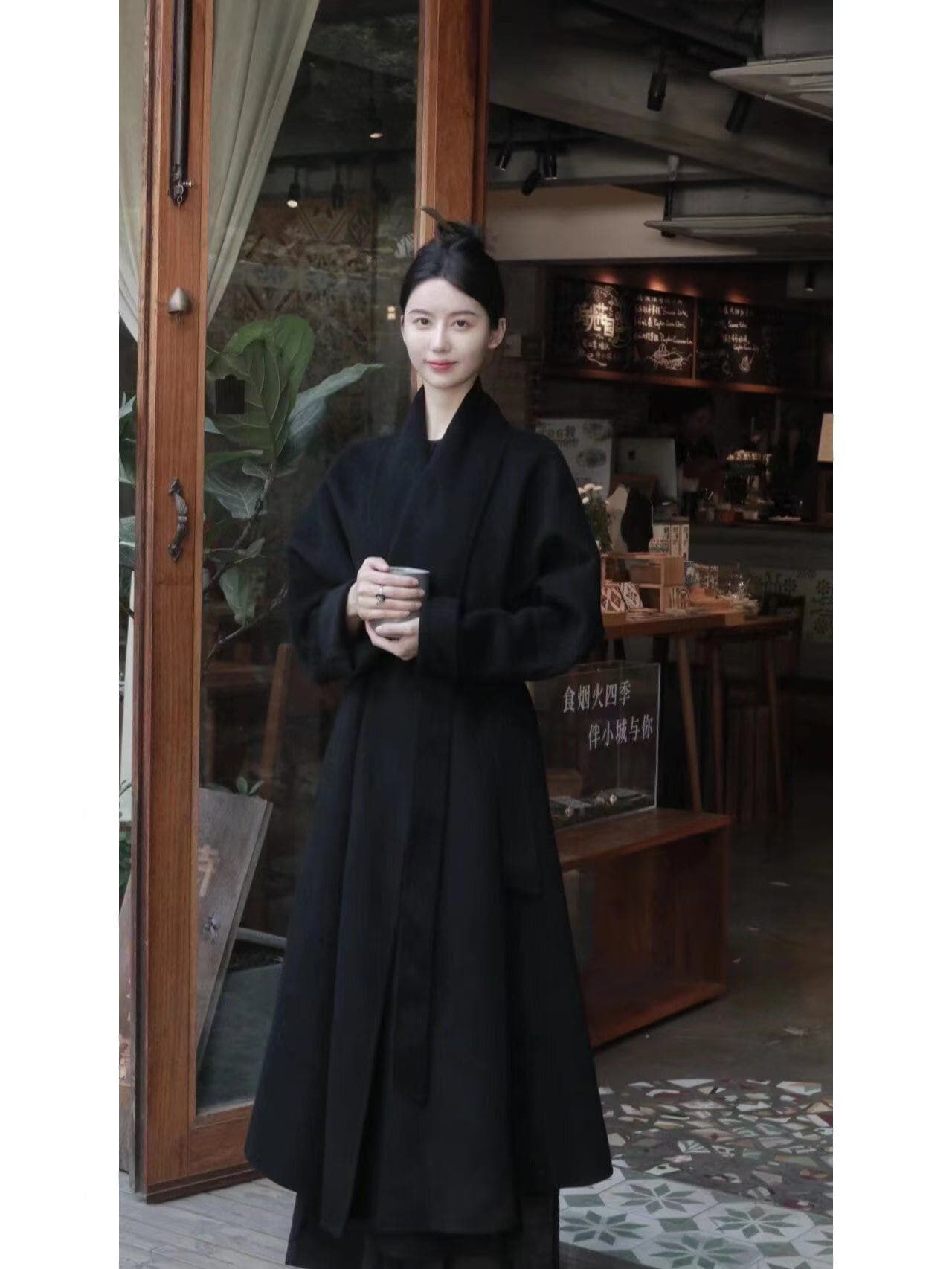 Model in a black cashmere coat at the entrance of a cafe.